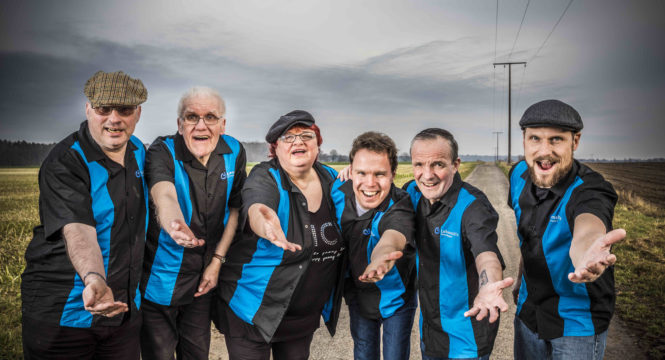 6 Mitglieder der Band Poppig Blue Cars vor einem bewölkten Himmel, alle in den gleichen schwarzen Hemden mit blauen Längsstreifen. Alle strecken die Hände einladend nach vorne aus