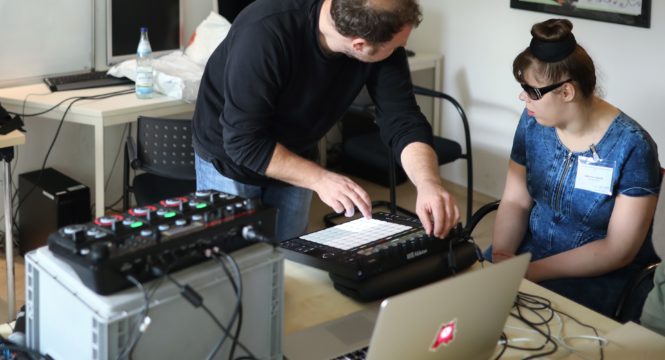 Ein Mann arbeitet an einem elektronischen Mischpult, eine Frau mit Sonnenbrille hört konzentriert zu - daneben ein Laptop und weiteres Mischpult