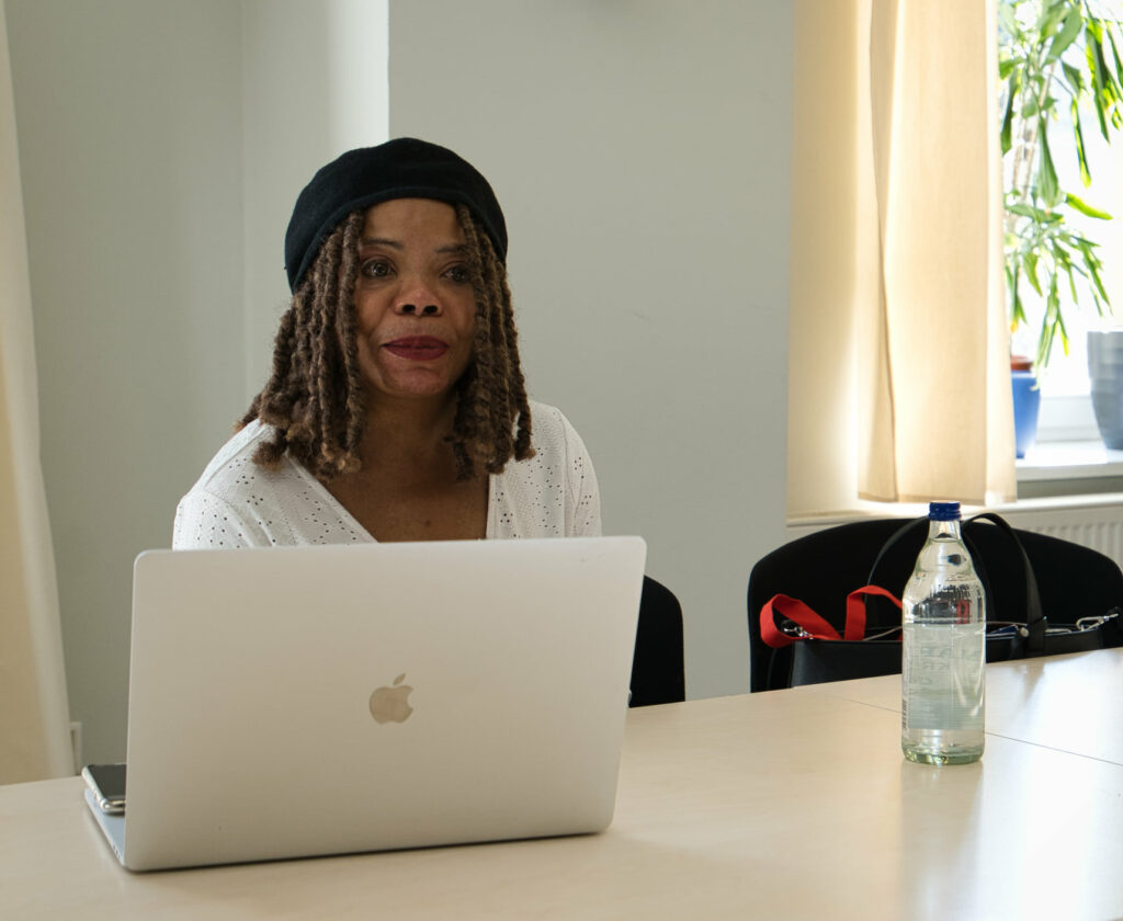 Marie, (die Leiterin des Leichte Sprache Workshops) mit Laptop und Wasser am Tisch sitzend