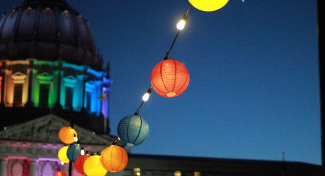 Im Vordergrund eine bunte Lichterkette mit kleinen Lampions, im Hintergrund unscharf die Kuppel des Berliner Doms