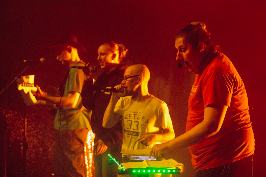 Vier Mitglieder der Band live beim Auftritt im orangenen Licht