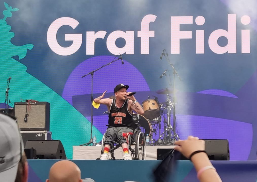 Ein Rapper im Rollstuhl Live auf einer Bühne, davor Publikum