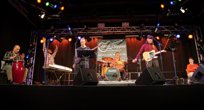 Foto von sechs Mitgliedern der Band live auf der Bühne