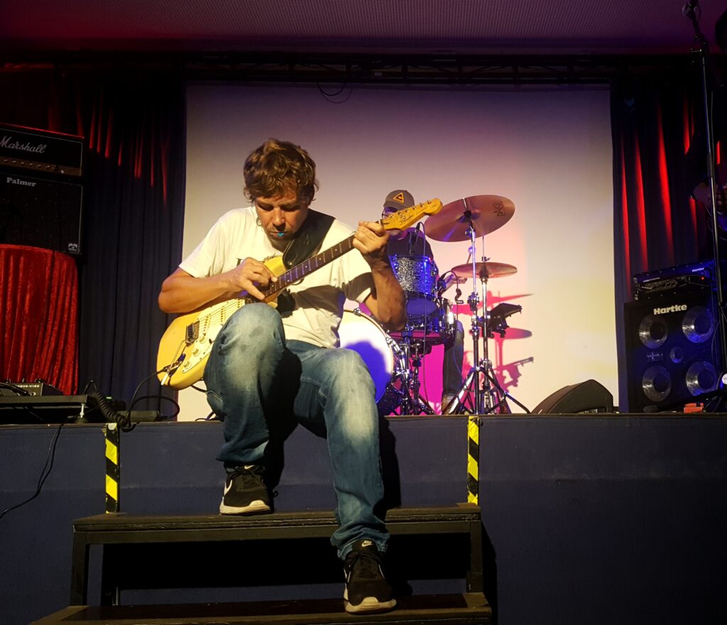 Der Gitarrist Mischa Gohlke sitzt auf einer Treppe zur Bühne und spielt ein Gitarrensolo