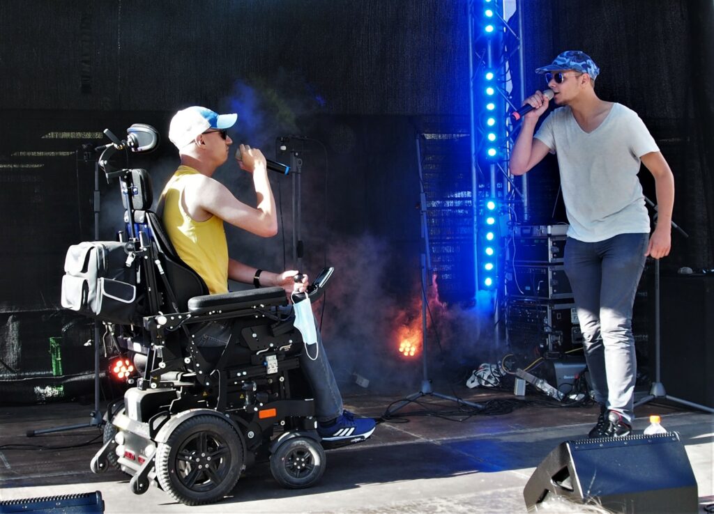 Ein Rap Duo in Erfurt auf der Bühne. Vorn ein Rapper im Rollstuhl, hinter ihm sein Kollege. Beide tragen Basecaps und singen ins Mikrofon.