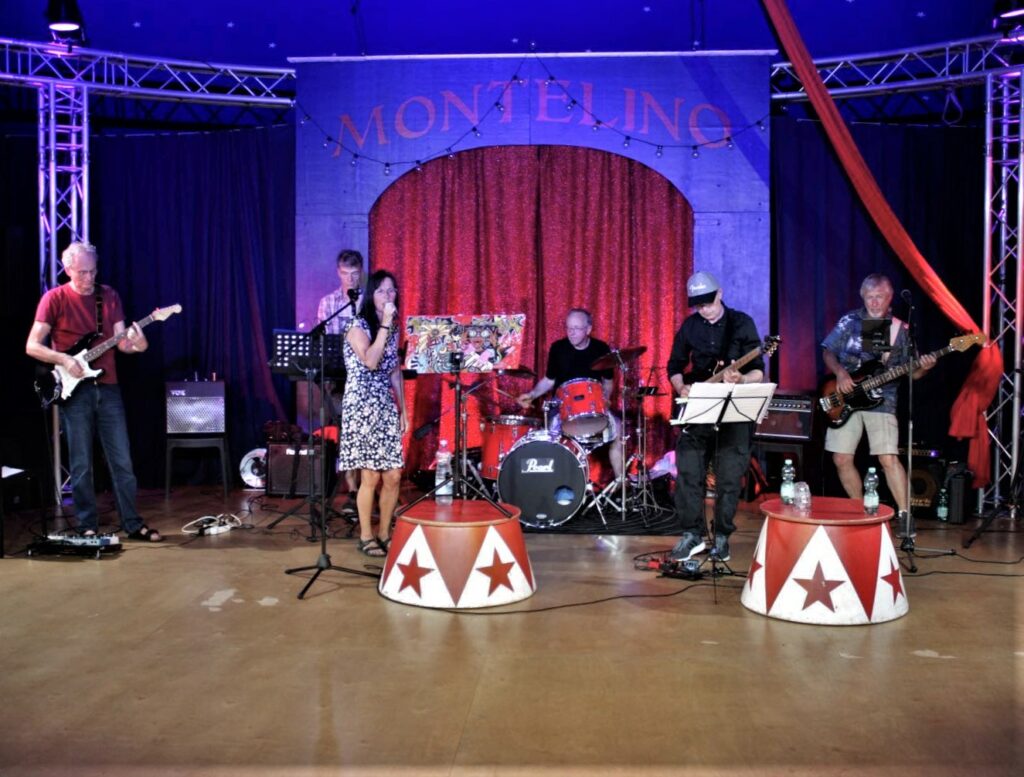 Farbfoto zeigt die sechsköpfige Band Funky Freaks im Zelt. Eine Frau singt.
