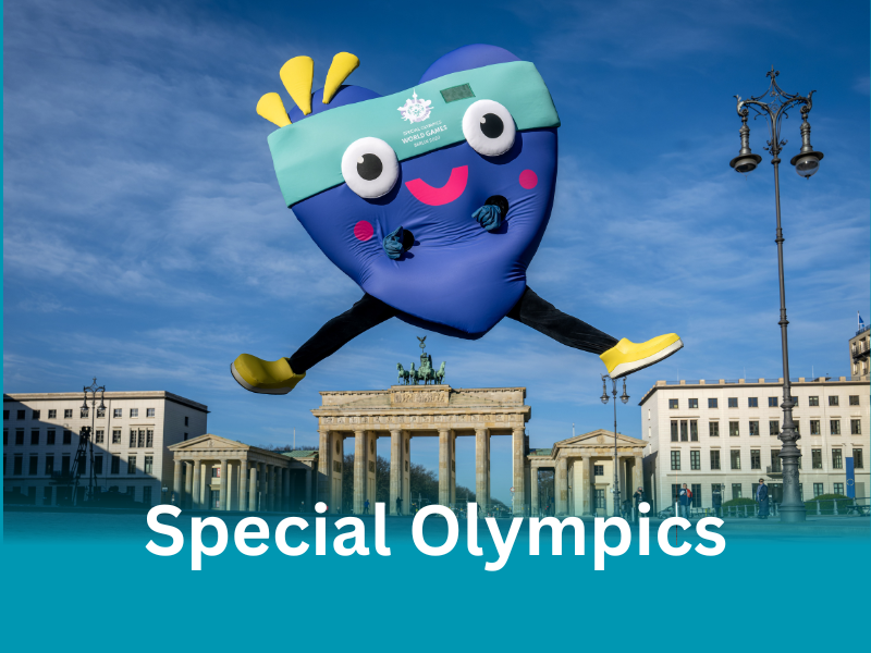 Das herzförmige blaue Maskotchen mit einem türkisen Stirnband und gelben Schuhen der Special Olympics World Games spingt vor dem Brandenburger Tor in die Luft.