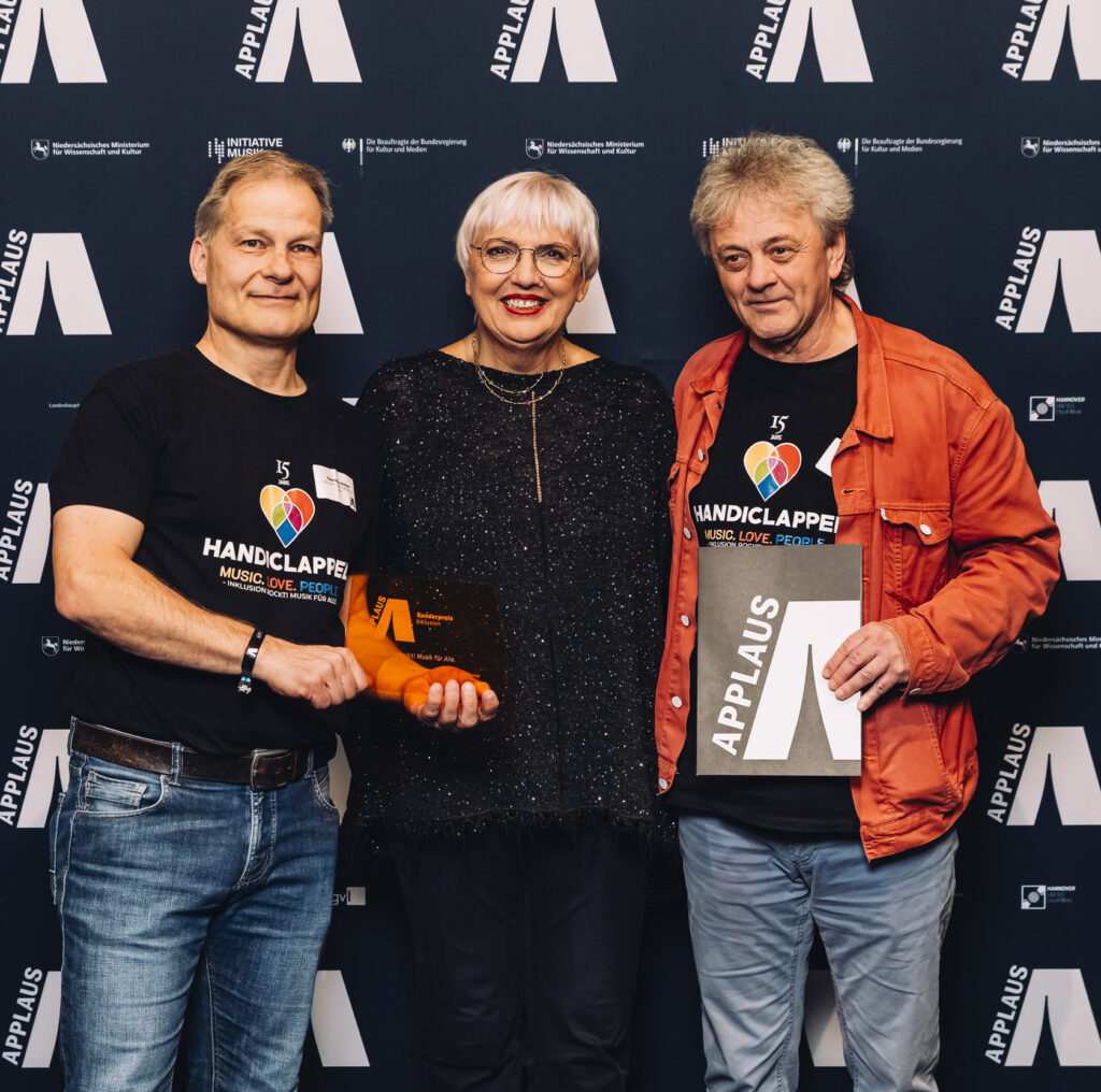Foto mit drei Personen, von rechts nach links, Peter Mandel, Claudia Roth und Thorsten Hesse, vor APPLAUS Fotowand