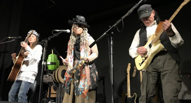 foto von zwei Frauen und einem Mann mit Gitarre und E-Gitarre und Gesang live beim Auftritt auf einer Bühne (innen)