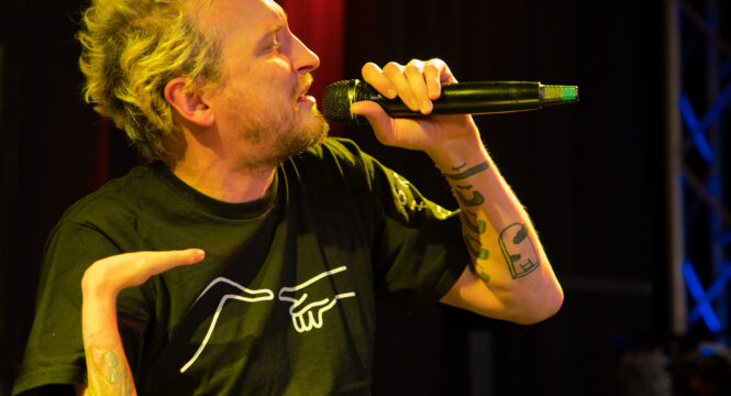Ein Portrait des Musikers Graf Fidi auf der Bühne. Er singt ins Mikofon.