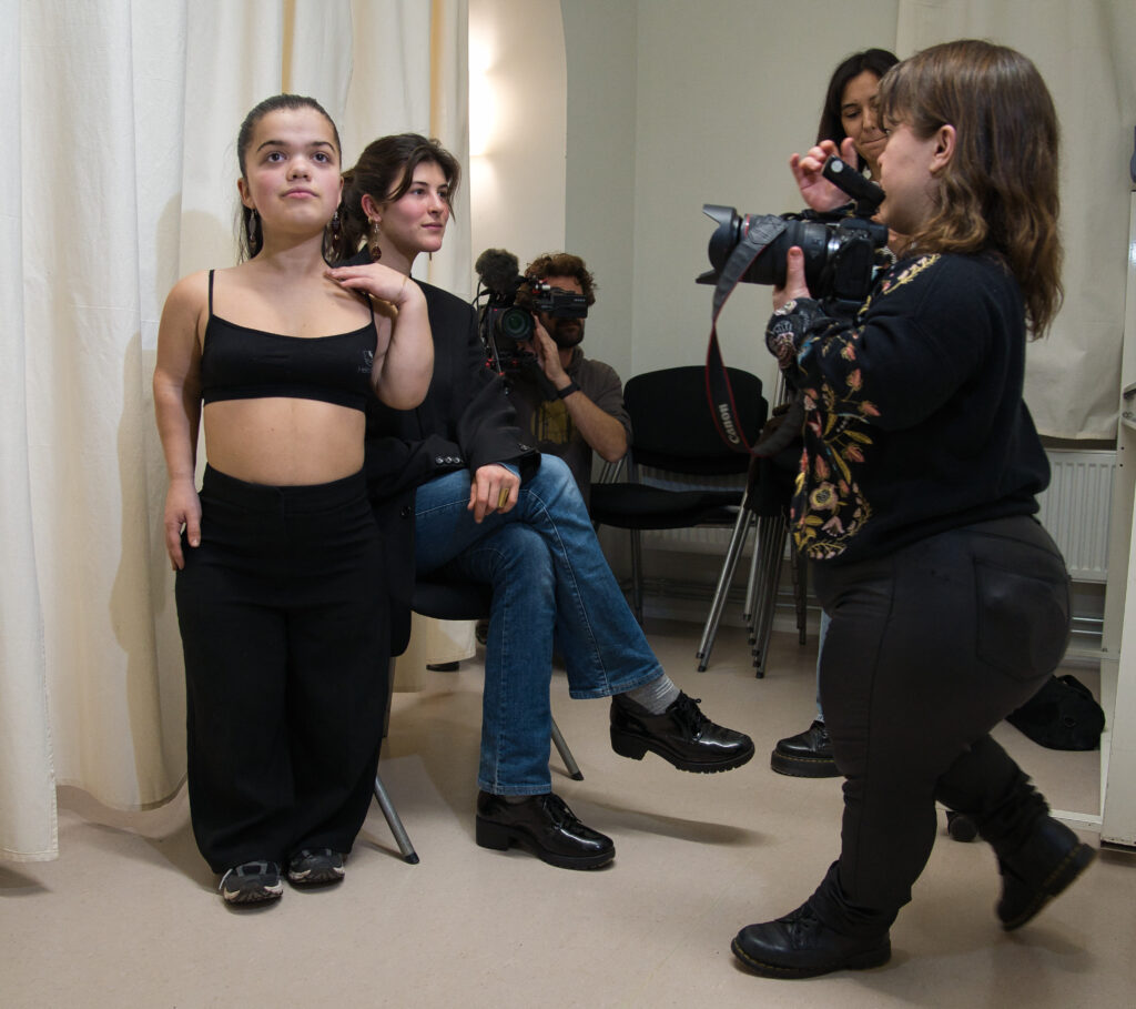 Mode und Musik Workshop: Ein Photoshooting, 2 Models präsentieren angefertigten Schmuck, rechts die Fotografin und im Hintergrund kniet ein Kameramann.