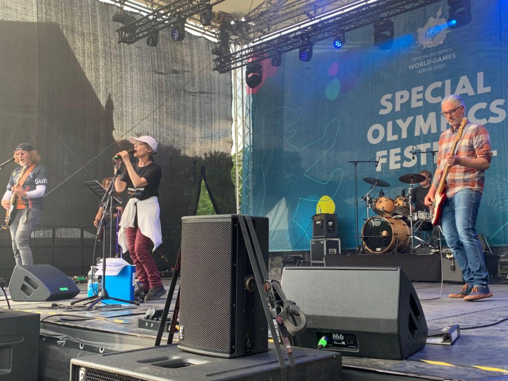 Vier Mitglieder der Band Rockantrieb auf einer großen Bühne, im Hintergrund groß ein Banner mit Aufschrift "Special Olympics"