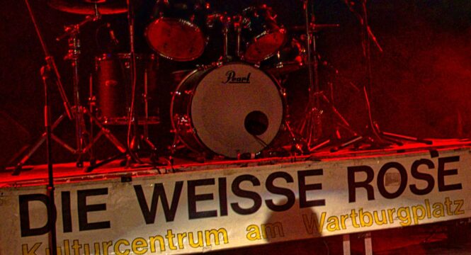 eine Bühne mit Schlagzeug, unten ist ein Banner mit der Aufschrift : Die Weisse Rose , Jugendzentrum am Wartburgplatz angebracht