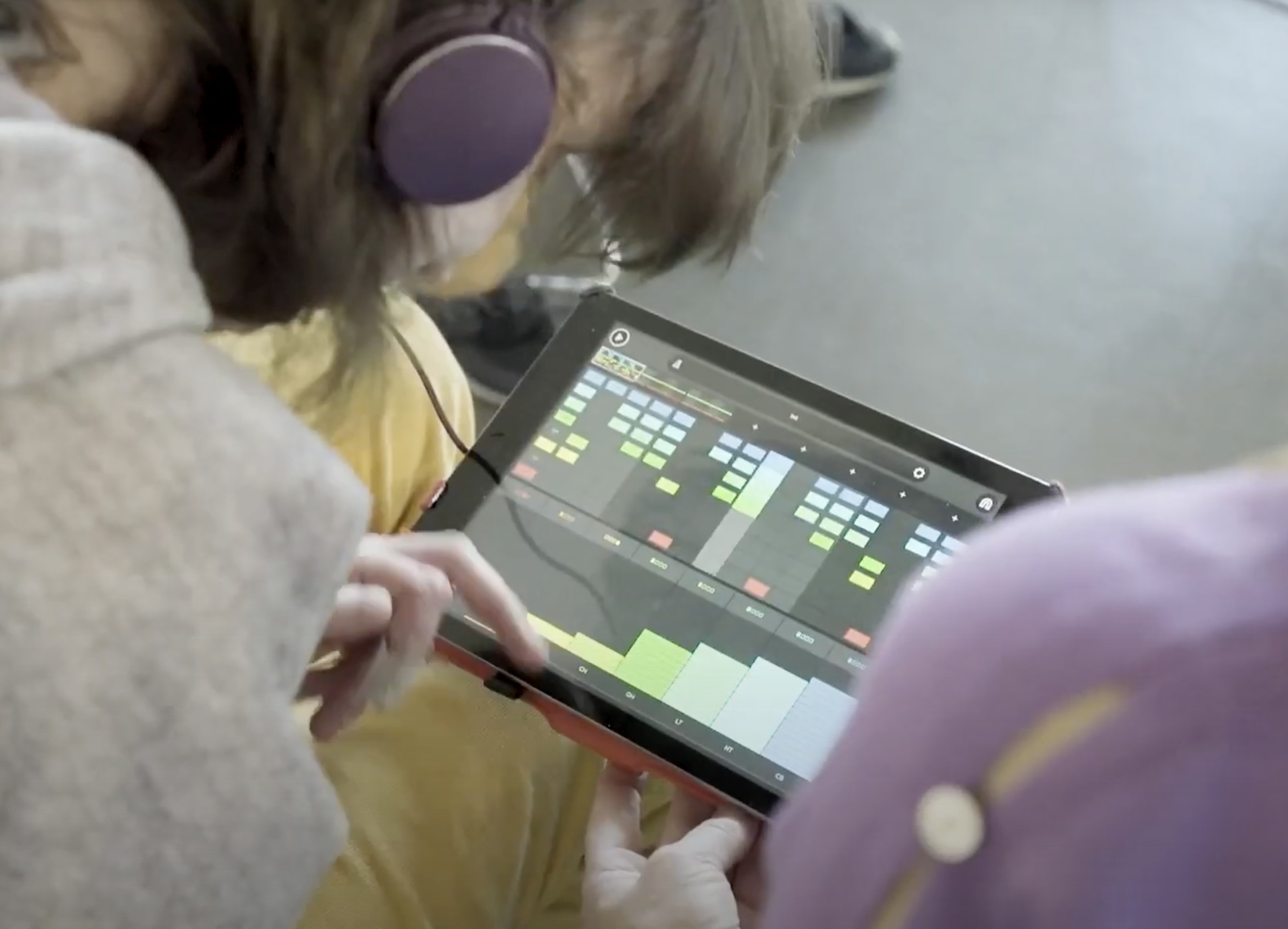 Foto von Person mit Kopfhörer, die auf einem iPad arbeitet, darauf bunte Grafiken vom Musikmachen