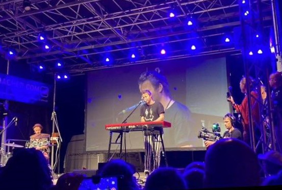 Beranger am Keyboard auf der Bühne, hinter ihm eine Filmleinwand , blaues Bühnenlicht