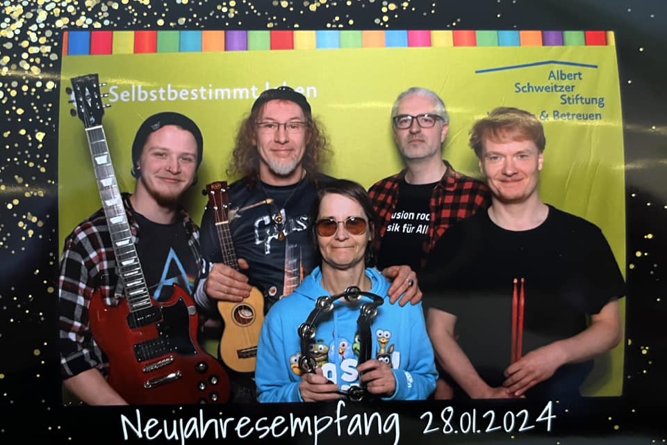 Ein Gruppenfoto von den fünf Mitgliedern von RockAntrieb vor einer gelben Wand, mit E-Gitarre und Ukulele. Dazu Schrift "Neujahrsempfang 28.01.2024" und Logo der Albert Schweitzer Stiftung.