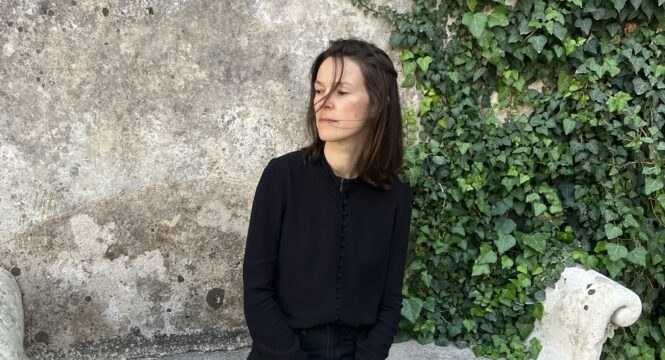 Toni Kater sitzt vor einer Wand, rechts von ihr rankt Efeu hoch