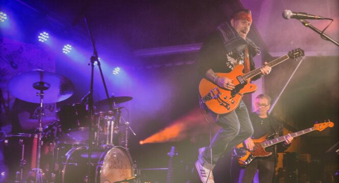 der Gitarrist von Crazy Dogs springt mit der Gitarre von der Bühne, viel buntes Bühnenlicht