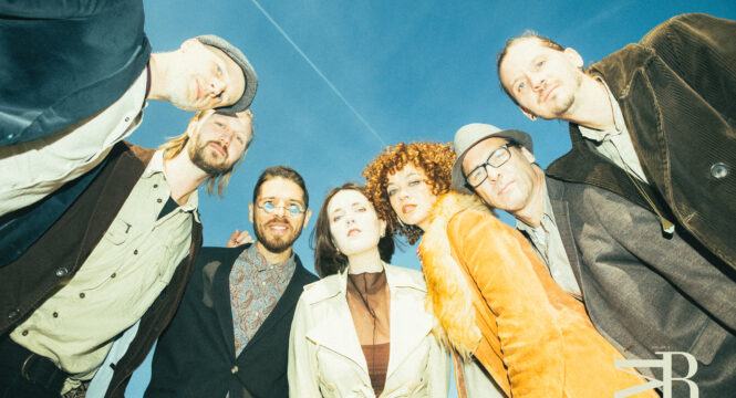 5 Musiker und 2 Musikerinnen der Band stehen im Halbkreis und schauen nach unten in die Kamera