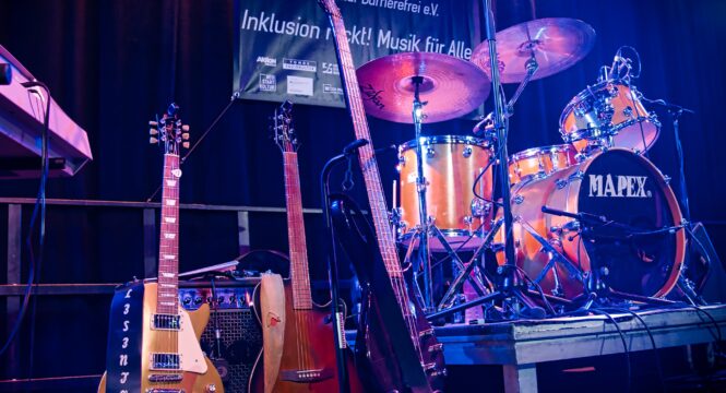 Gitarren und ein Schlagzeug ohne Musiker auf der Bühne, im Hintergrund das Handiclapped Banner