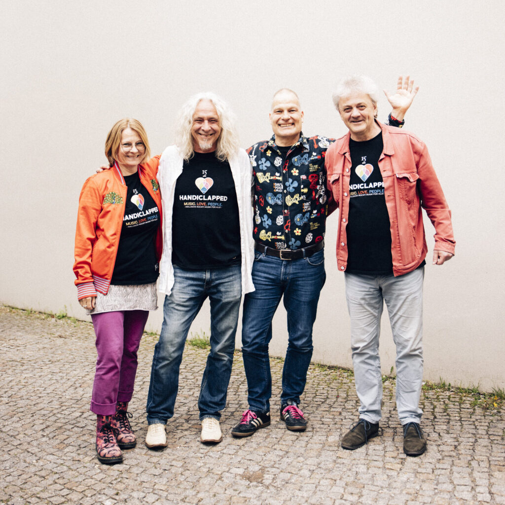 das Handiclapped Team im Gruppenfoto: Jana, Jens, Thorsten und Peter. Alle lächeln in die Kamera, Thorsten winkt mit einer Hand