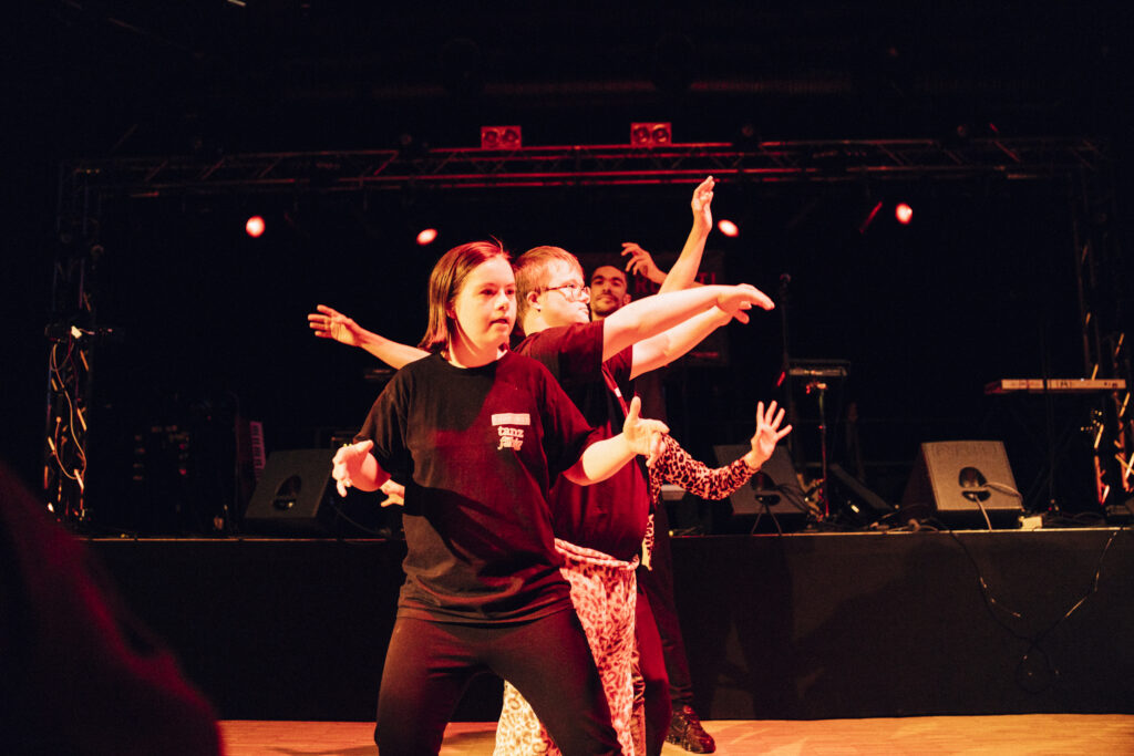 Tänzer:innen bei ihrer Aufführung. Sie stehen in einer Reihe hintereinander, man sieht nur 3 Gesichter aber viele Arme in alle Richtungen ausgestreckt