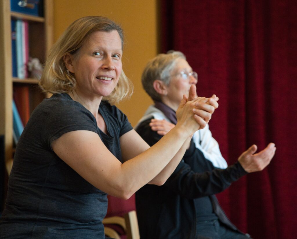 Buntfoto von zwei Frauen, die klatschen. Die vordere der beiden guckt in die Kamera.

