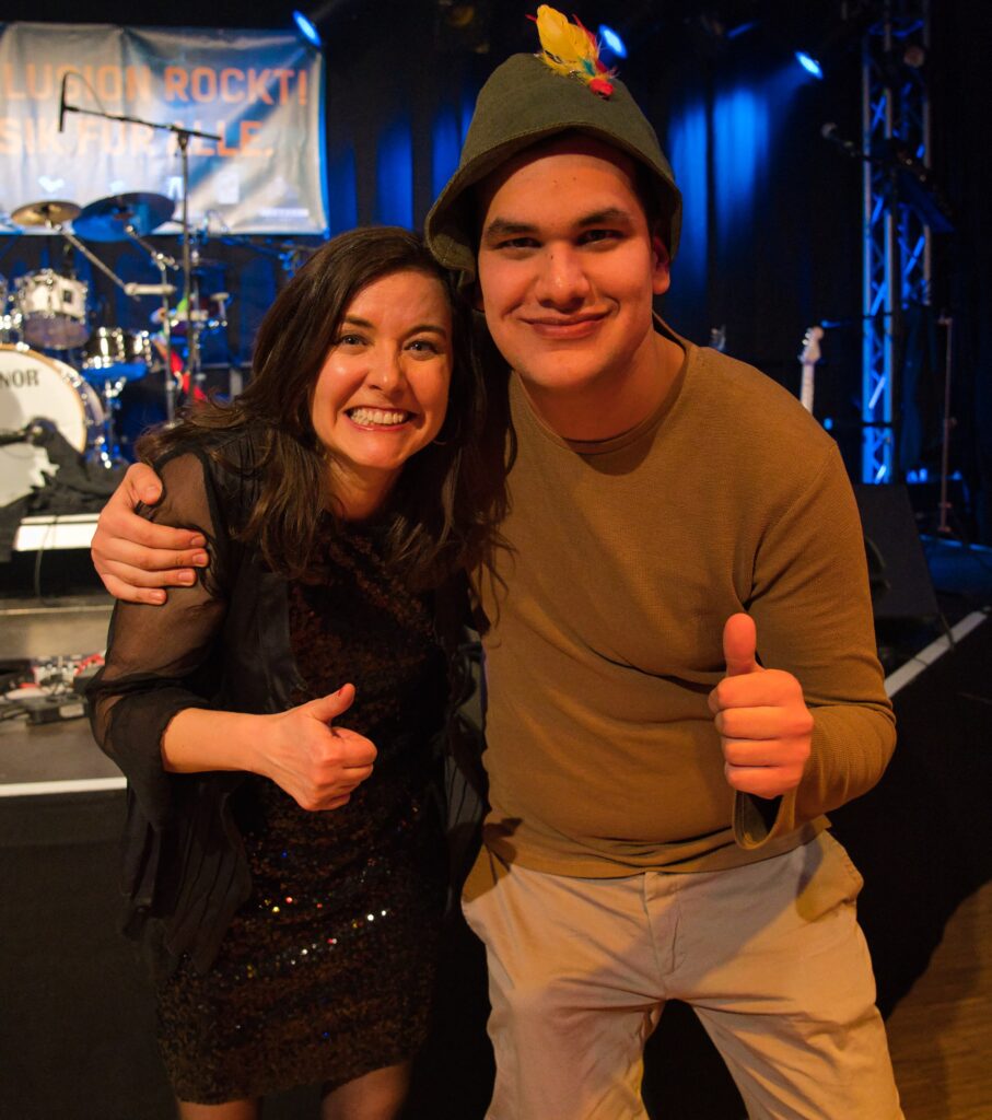 die Sängerin im Arm eine jungen Mannes aus dem Publikum vor der Bühne. Beide lachen und machen die "Daumen hoch" Geste