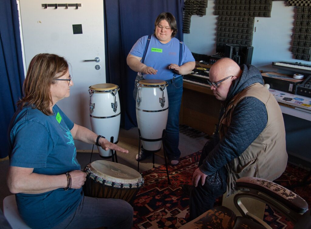 3 Workshopteilnehmer:innen, 2 Frauen und ein Mann trommeln auf Djembe und Congas