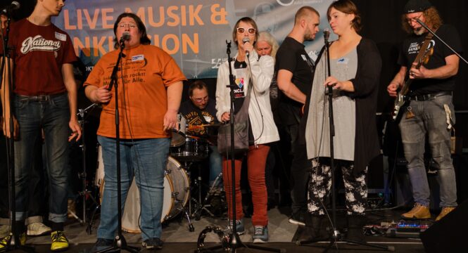 Ein Bandworkshop: auf einer großen Bühne stehen 8 Workshopteilnehmer*innen und musizieren mit Mikros für Gesang, SChlagzeug, Gitarre und Bass