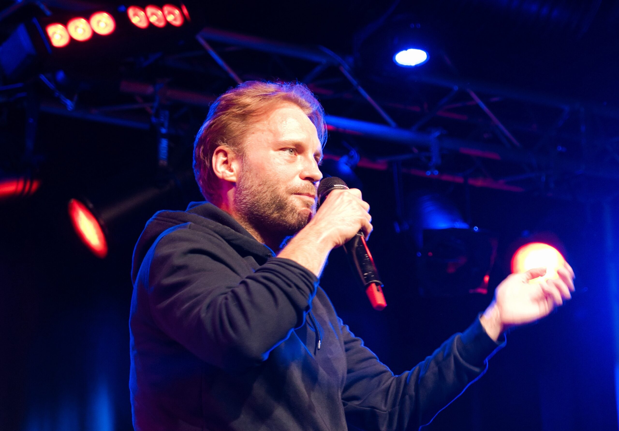 Buntfoto von Luis Lyrisch. Er steht auf einer Bühne und singt in ein Mikrofon. 